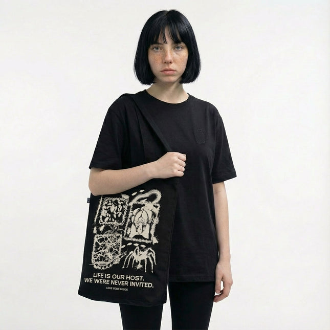 zdjęcie przedstawie modelkę z czarną torbą bawełnianą na zakupy. Torba ma maksymalistyczną białą grafikę z motywami body horror.