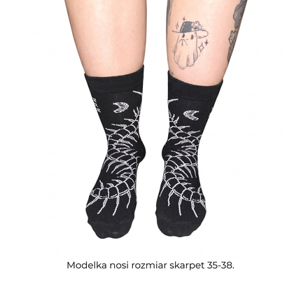 Osoba ma na stopach czarne długie bawełniane skarpety z motywem skolopendry od Love Your Inside. Modelka nosi rozmiar skarpet 35–38.